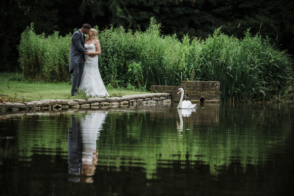 Bride and groom reflected in lake with swan